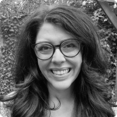 Black and white image of Amber Piriano wearing glasses and smiling at the camera