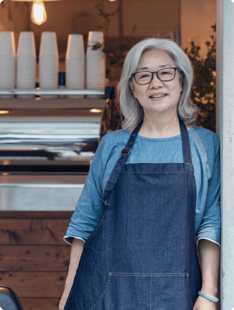 Lifestyle image of member in an apron at a cafe, leaning against door frame.