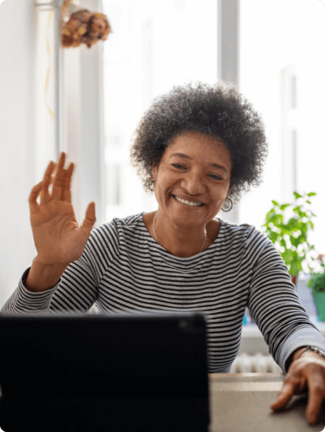 Senior woman waving and smiling at her computer screen.