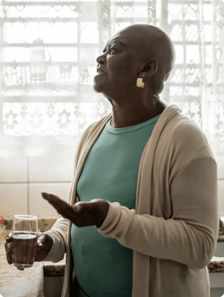 Senior woman with water in one hand and medication in another.