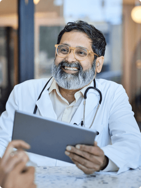 Doctor smiling and talking to a person while holding a tablet device.