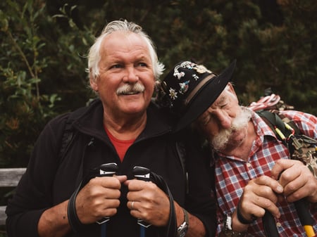 Two men sitting together outdoors, one leaning on other
