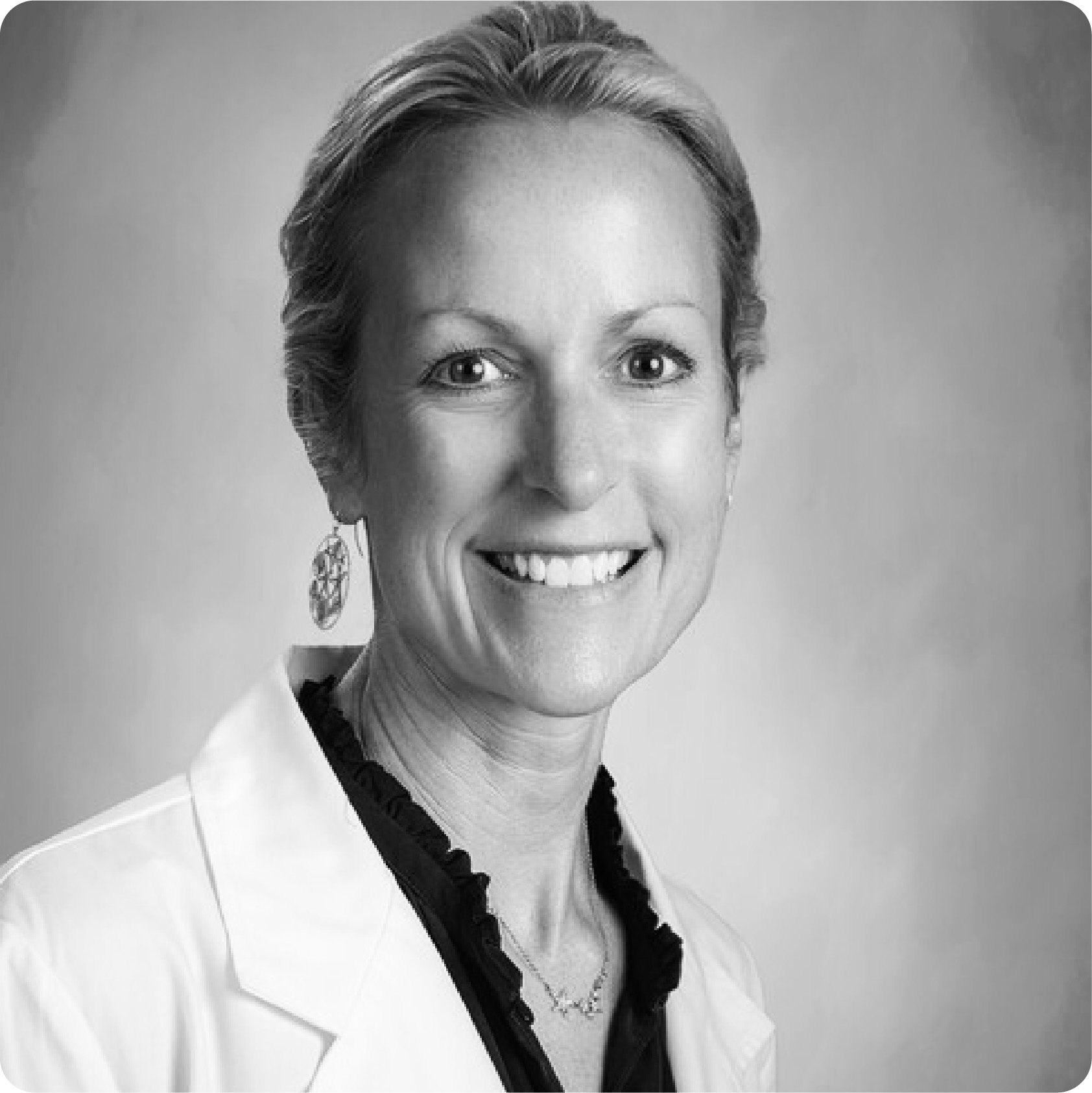 Black and white image of Katie Caton wearing a white jacket and smiling at the camera