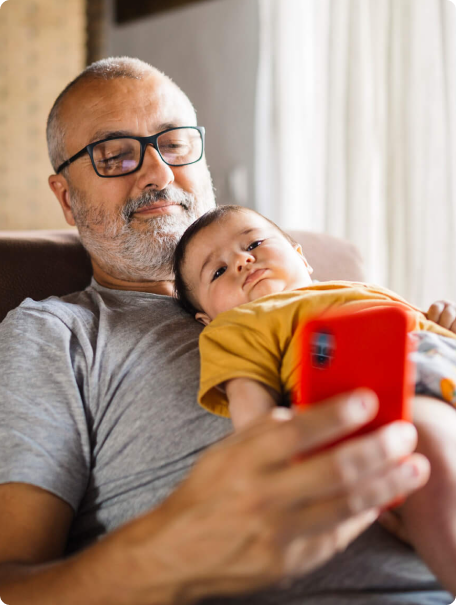 A man holds a baby close while intently gazing at his cell phone