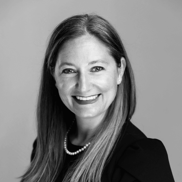 Black and white image of Cora Beth Enzor wearing a pearl necklace and black blouse, smiling at the camera