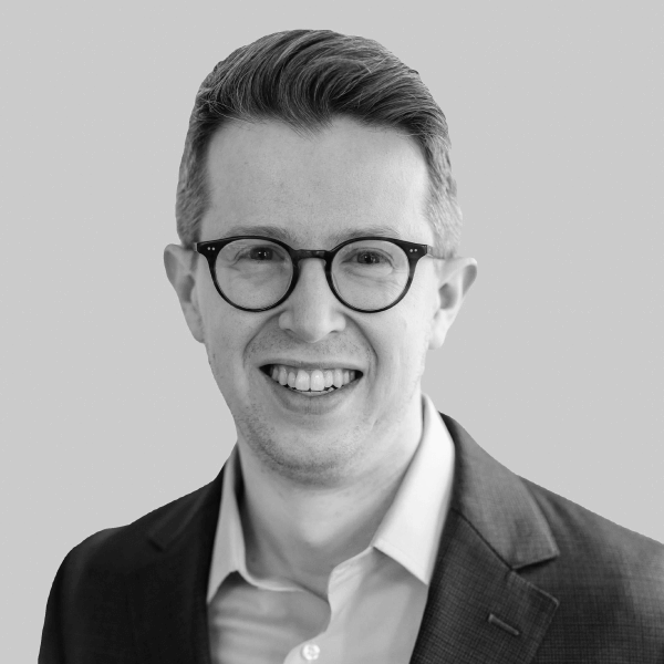 Black and white photo of Etan Raskas wearing round glasses and smiling at the camera